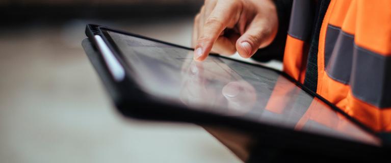 Person in Warnweste bedient ein Tablet.