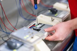 Hände montieren einen Stromzähler mit Schraubendreher.