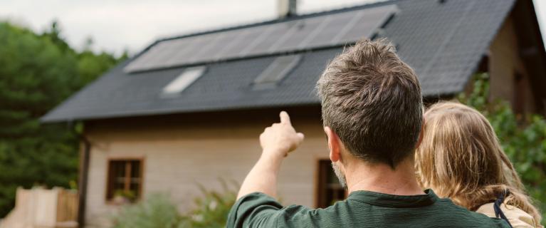 Mann mit Kind zeigt auf Solaranlage auf Hausdach.