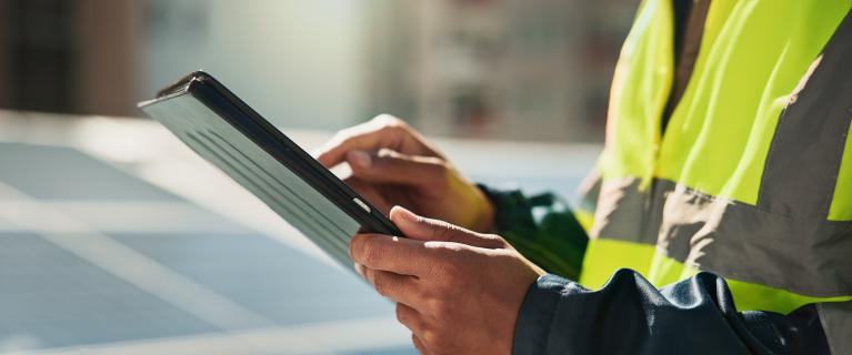 Person in Warnweste bedient ein Tablet vor Solarmodulen.