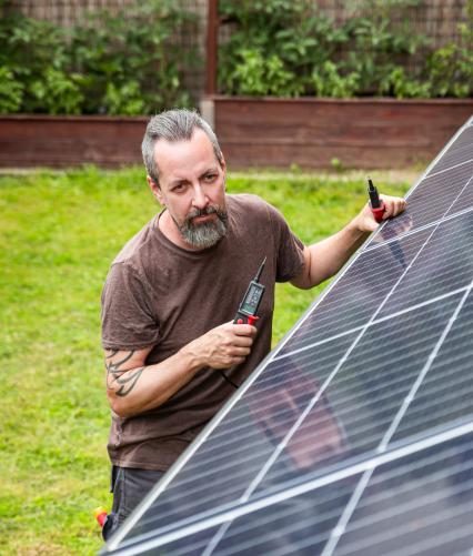 Mann inspiziert Solarmodul im Garten.