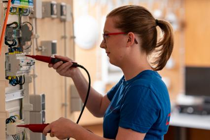 Technikerin prüft Schaltschrank mit Messgerät.
