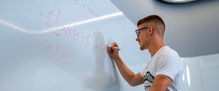 Mann schreibt Formeln an ein Whiteboard.