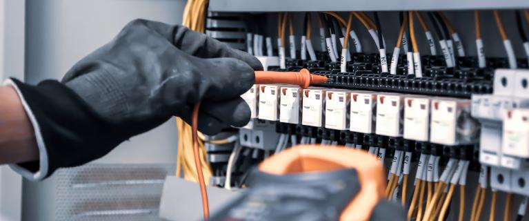 Hand mit Messspitze prüft Anschlüsse in einem Schaltschrank.