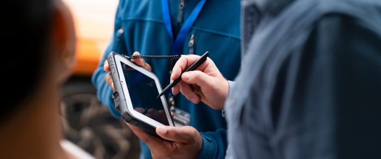Personen besprechen etwas am Tablet, eine Hand zeigt mit Stift auf den Bildschirm.
