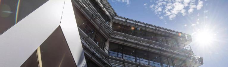 Stadtwerke Karlsruhe Netzservice GmbH Aufnahme von unten des modernen Glas- und Stahlgebäudes der Stadtwerke Karlsruhe Netzservice. Rechts blendet die Sonne am blauen Himmel.