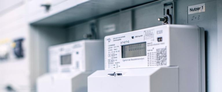 Reihe moderner Stromzähler in einem grauen Zählerschrank; vorne eine moderne Messeinrichtung mit einem Kommunikationsmodul.