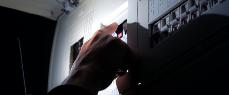 Hand schaltet Sicherungsautomaten im geöffneten Stromverteilerkasten.