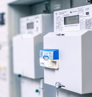 Reihe moderner Stromzähler in einem grauen Zählerschrank; vorne eine moderne Messeinrichtung mit einem Kommunikationsmodul.